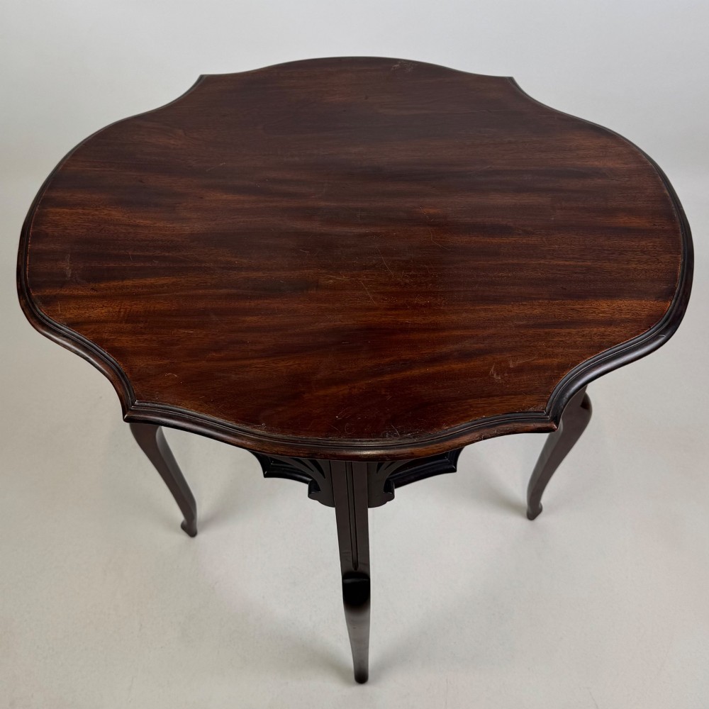 An Edwardian dark mahogany side table featuring a shaped top, pierced carved spandrels, slender cabriole legs, and a lower tier shelf. View VIII