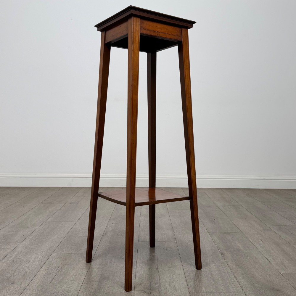 A tall, slender Edwardian satinwood plant stand with square tapered legs, a flat square top, and a lower undertier shelf. View VI