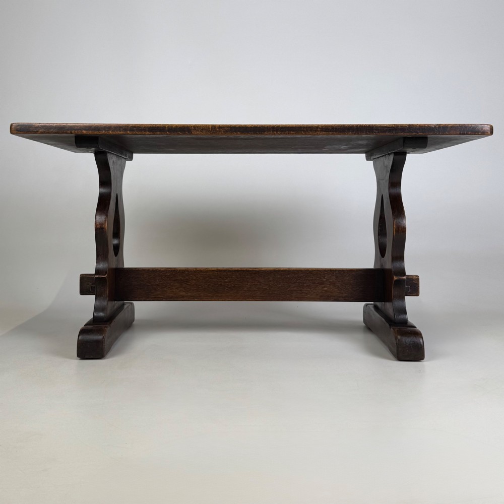 A dark oak trestle coffee table featuring shaped side supports with teardrop cut-outs and a low central stretcher.