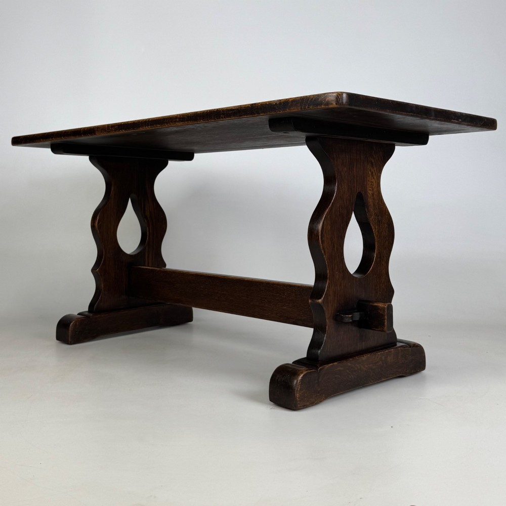 A dark oak trestle coffee table featuring shaped side supports with teardrop cut-outs and a low central stretcher. View II