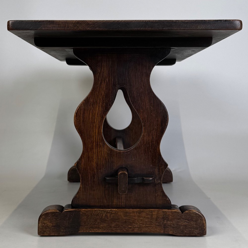 A dark oak trestle coffee table featuring shaped side supports with teardrop cut-outs and a low central stretcher. View VII
