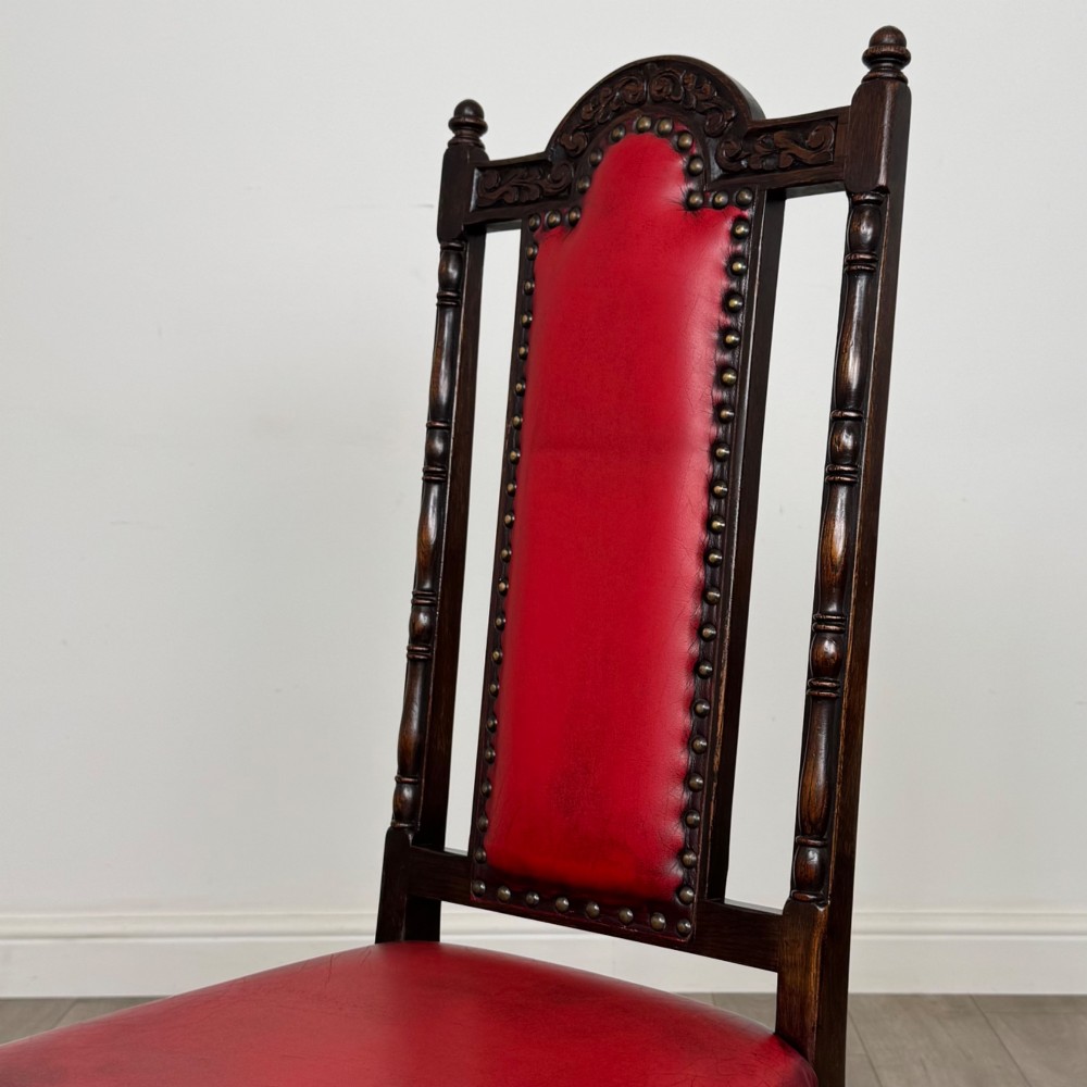 A set of six dark oak dining chairs featuring red leather upholstery, carved crests, turned legs, and brass stud trimming. View V