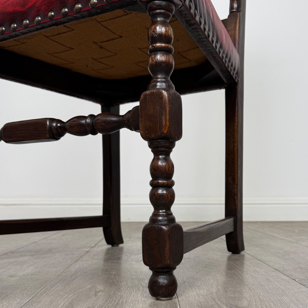 A set of six dark oak dining chairs featuring red leather upholstery, carved crests, turned legs, and brass stud trimming. View VII