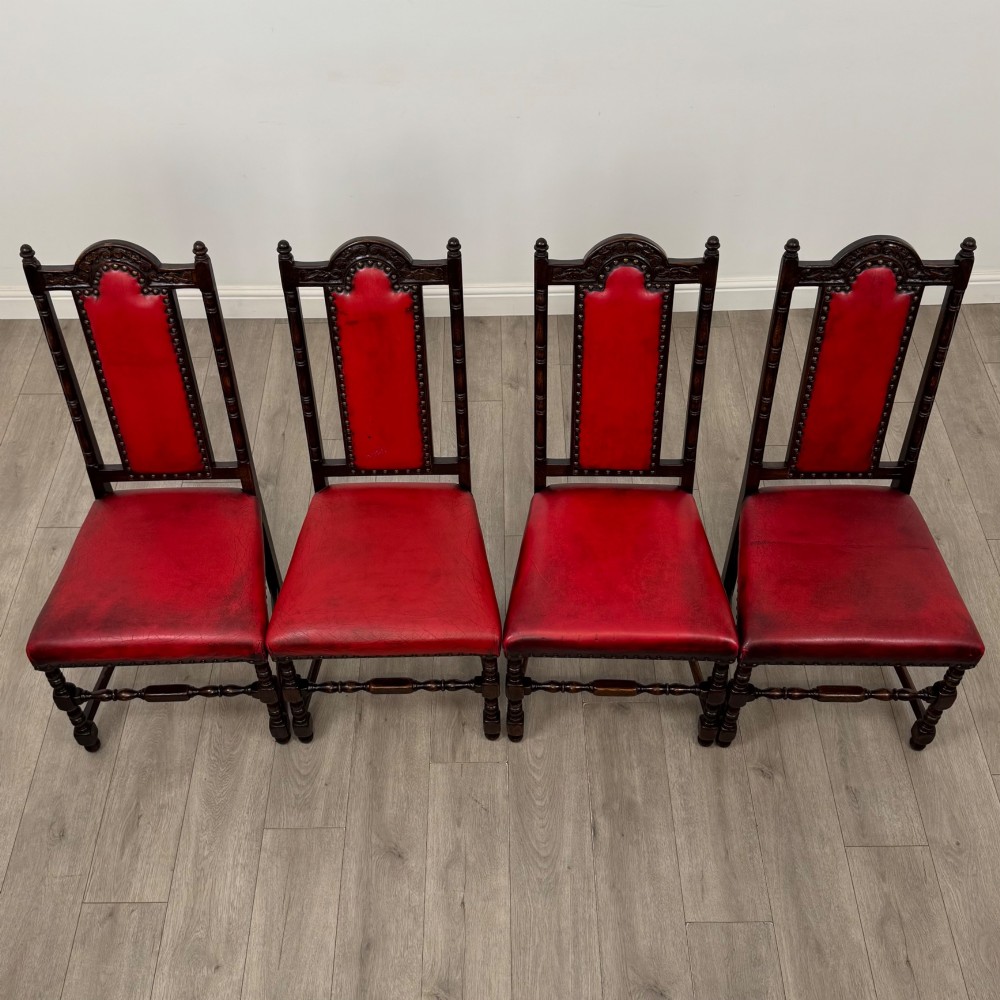 A set of six dark oak dining chairs featuring red leather upholstery, carved crests, turned legs, and brass stud trimming. View VIII