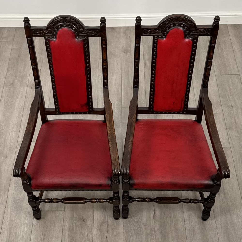 A set of six dark oak dining chairs featuring red leather upholstery, carved crests, turned legs, and brass stud trimming. View IX