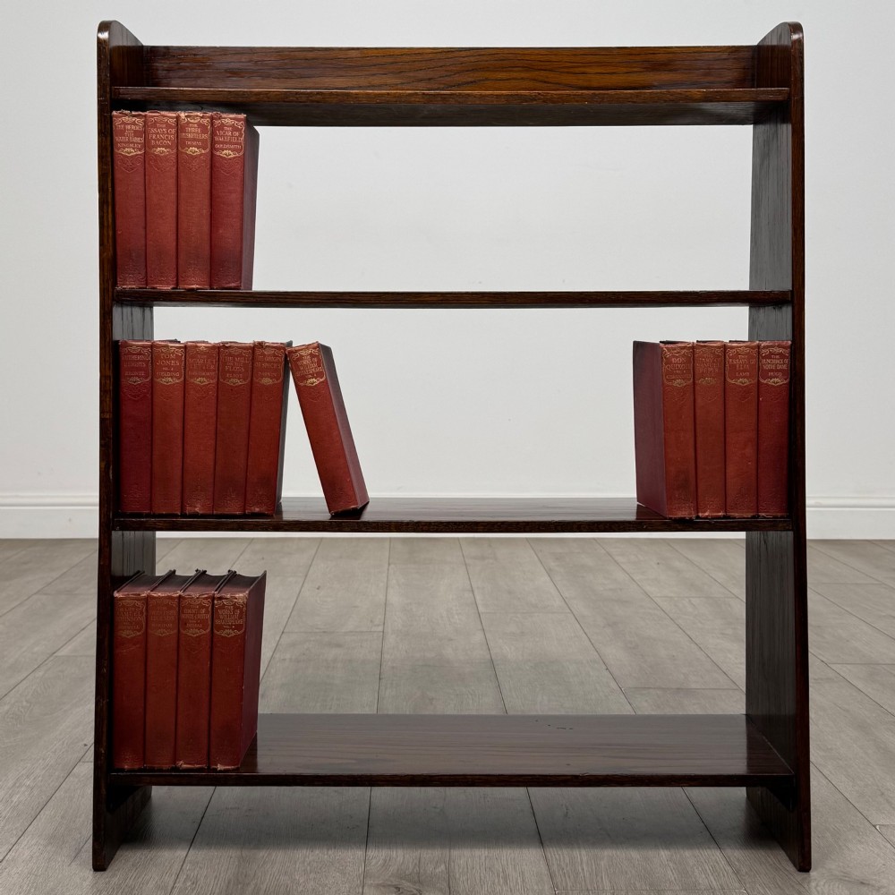 A dark oak Edwardian open bookcase with four horizontal shelves holding leather-bound books.