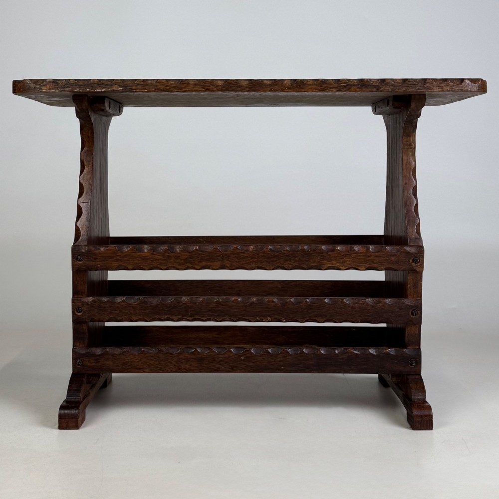 A dark brown oak side table featuring a rectangular top with scalloped carved edges over an integrated three-slat magazine rack below.