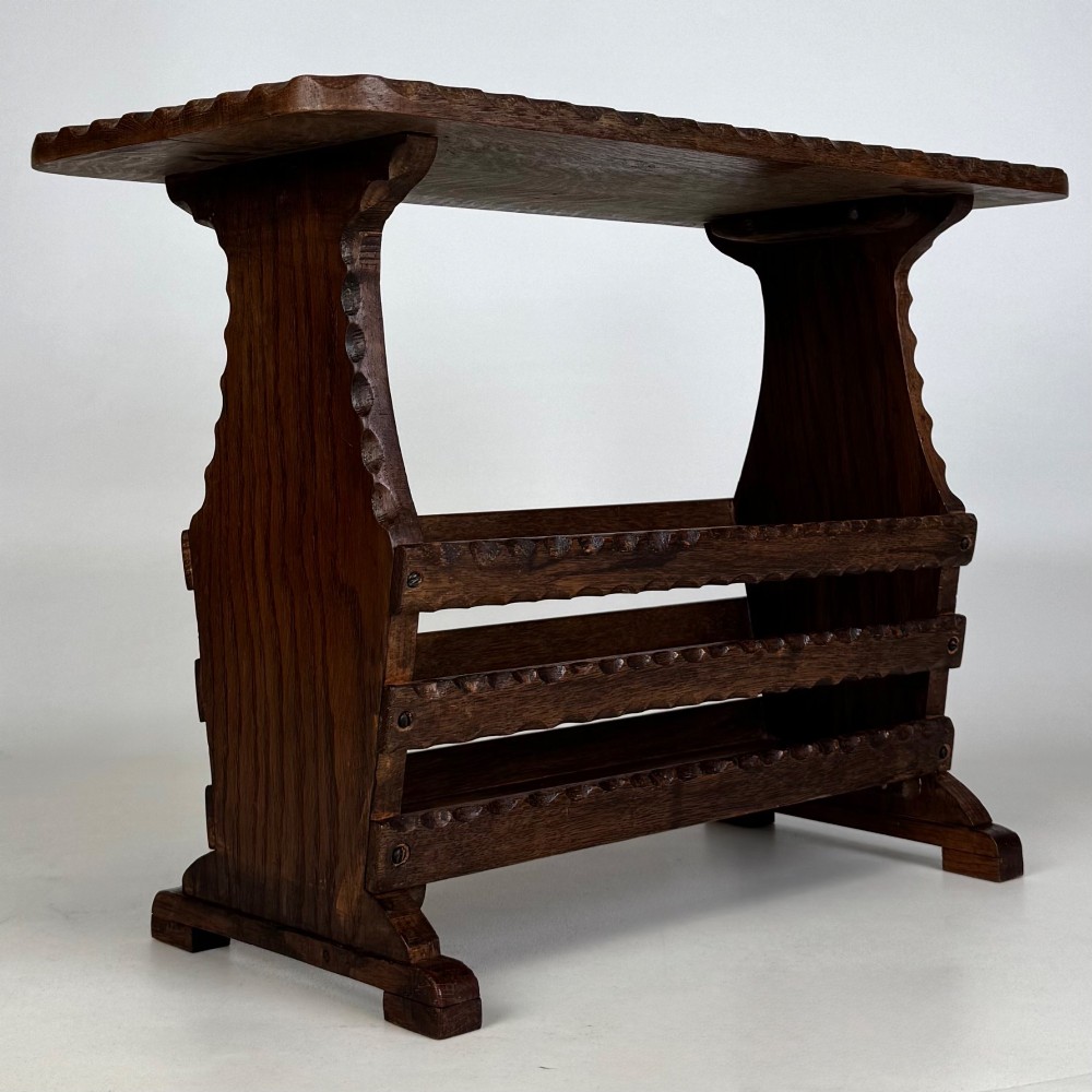 A dark brown oak side table featuring a rectangular top with scalloped carved edges over an integrated three-slat magazine rack below. View IV