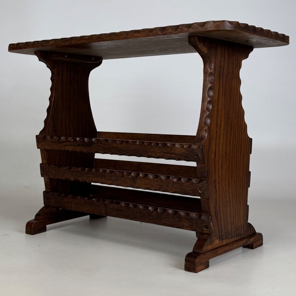 A dark brown oak side table featuring a rectangular top with scalloped carved edges over an integrated three-slat magazine rack below. View VI