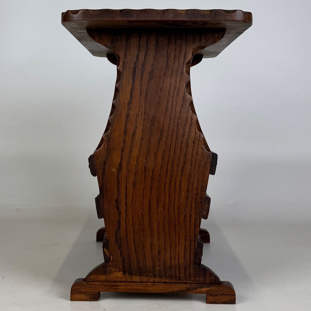 A dark brown oak side table featuring a rectangular top with scalloped carved edges over an integrated three-slat magazine rack below. View VII