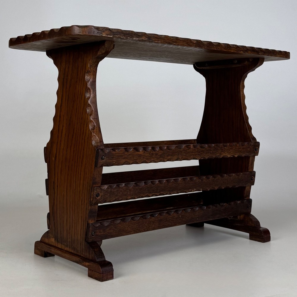 A dark brown oak side table featuring a rectangular top with scalloped carved edges over an integrated three-slat magazine rack below. View VIII