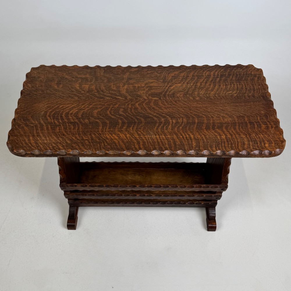 A dark brown oak side table featuring a rectangular top with scalloped carved edges over an integrated three-slat magazine rack below. View IX