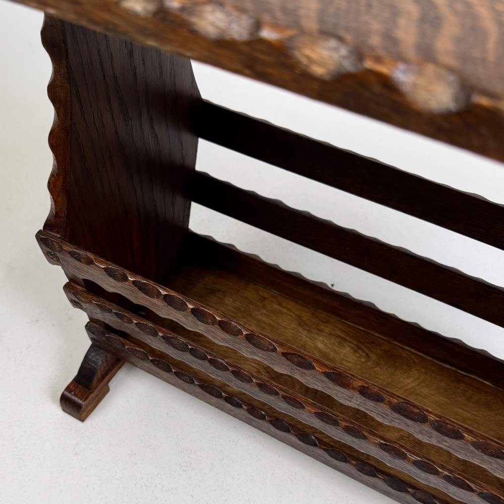 A dark brown oak side table featuring a rectangular top with scalloped carved edges over an integrated three-slat magazine rack below. View X