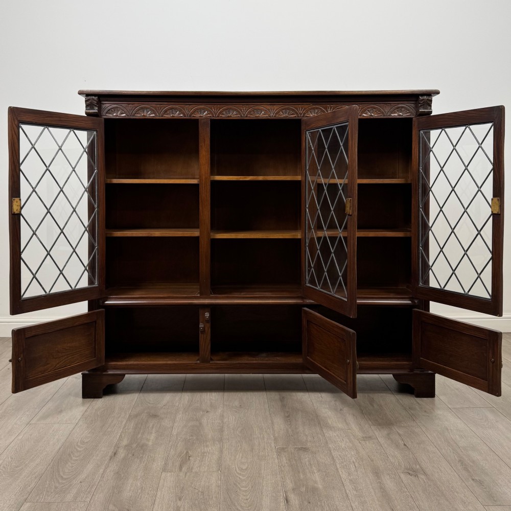A large dark brown carved oak display cabinet featuring three leaded glass doors over three carved cupboard doors with metal ring pulls. View II