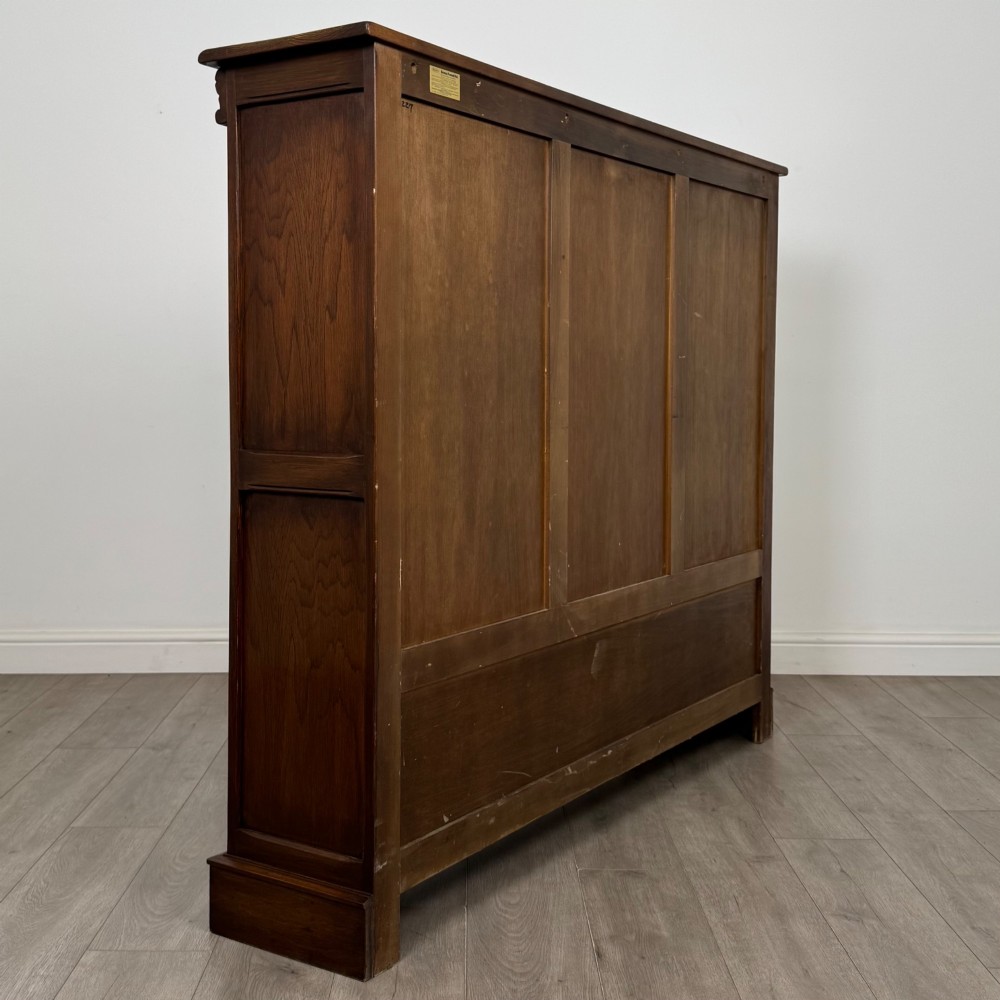 A large dark brown carved oak display cabinet featuring three leaded glass doors over three carved cupboard doors with metal ring pulls. View V