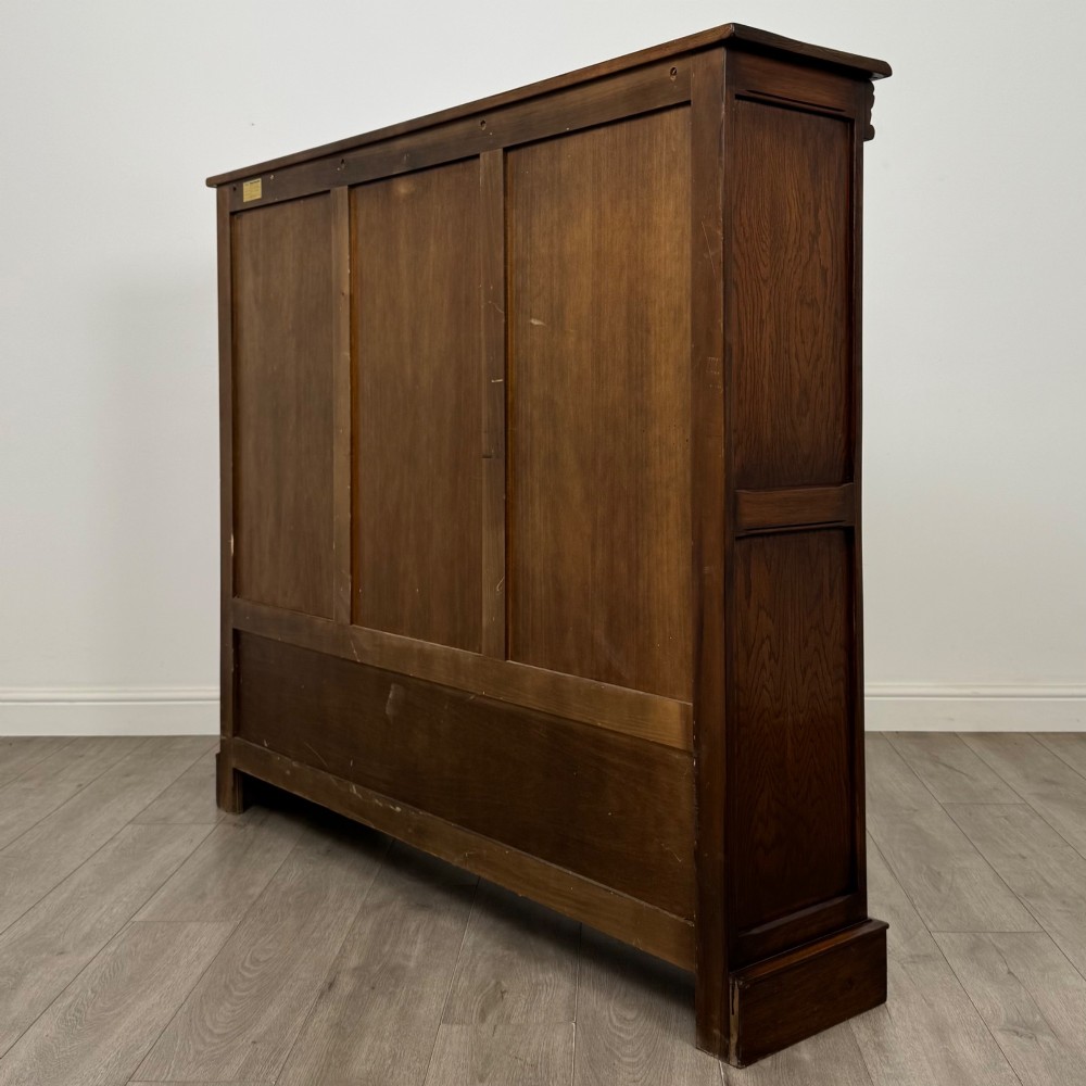 A large dark brown carved oak display cabinet featuring three leaded glass doors over three carved cupboard doors with metal ring pulls. View VII