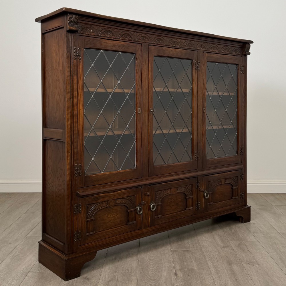A large dark brown carved oak display cabinet featuring three leaded glass doors over three carved cupboard doors with metal ring pulls. View IX