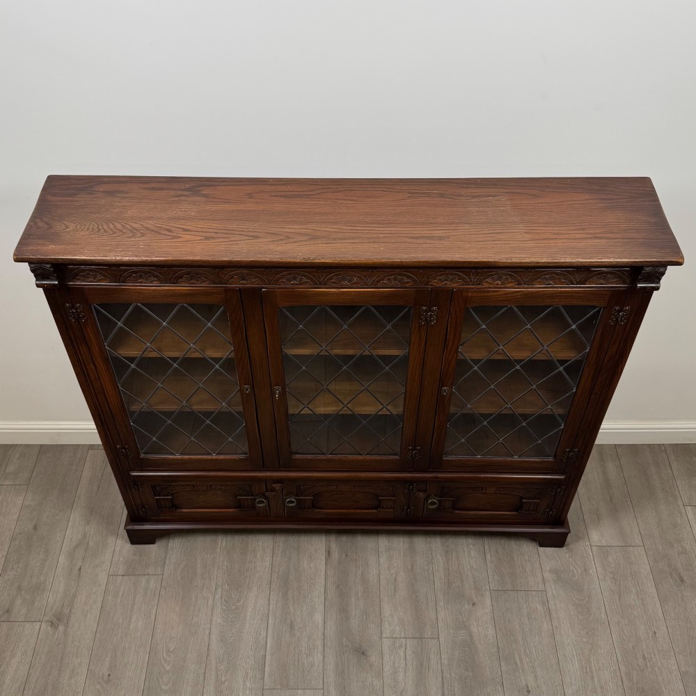 A large dark brown carved oak display cabinet featuring three leaded glass doors over three carved cupboard doors with metal ring pulls. View X