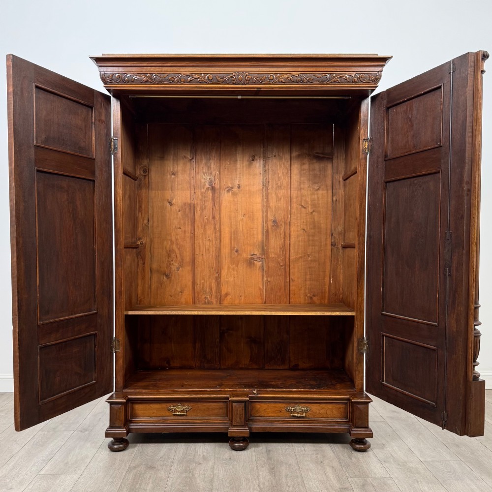 A 19th-century French walnut wardrobe with double doors featuring detailed carved foliate panels, central fluted columns, two lower drawers, and a stepped cornice. View II