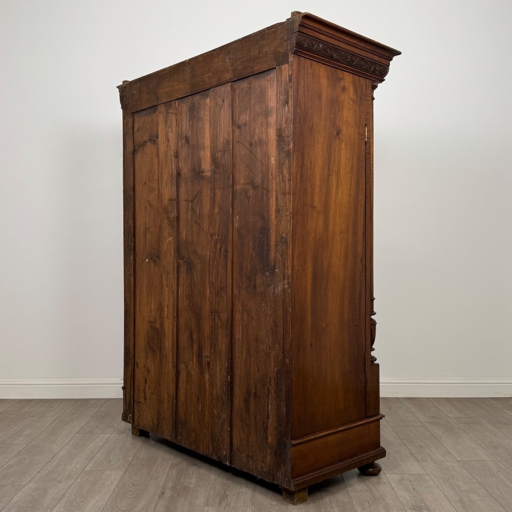 A 19th-century French walnut wardrobe with double doors featuring detailed carved foliate panels, central fluted columns, two lower drawers, and a stepped cornice. View VII