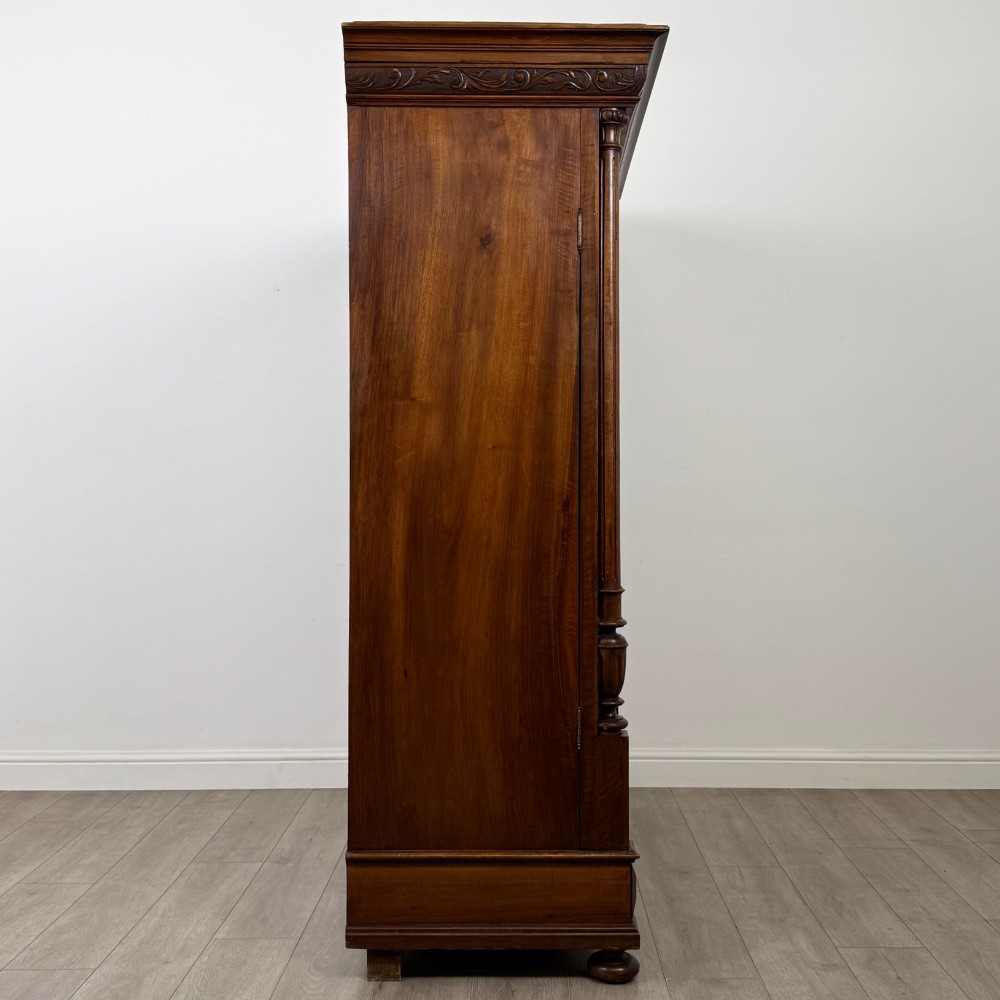 A 19th-century French walnut wardrobe with double doors featuring detailed carved foliate panels, central fluted columns, two lower drawers, and a stepped cornice. View VIII