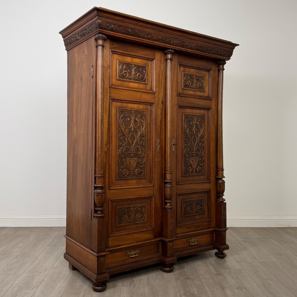 A 19th-century French walnut wardrobe with double doors featuring detailed carved foliate panels, central fluted columns, two lower drawers, and a stepped cornice. View IX
