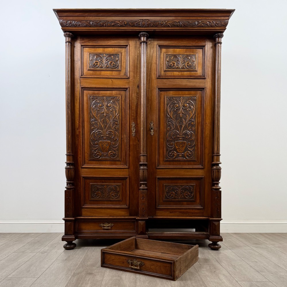 A 19th-century French walnut wardrobe with double doors featuring detailed carved foliate panels, central fluted columns, two lower drawers, and a stepped cornice. View X