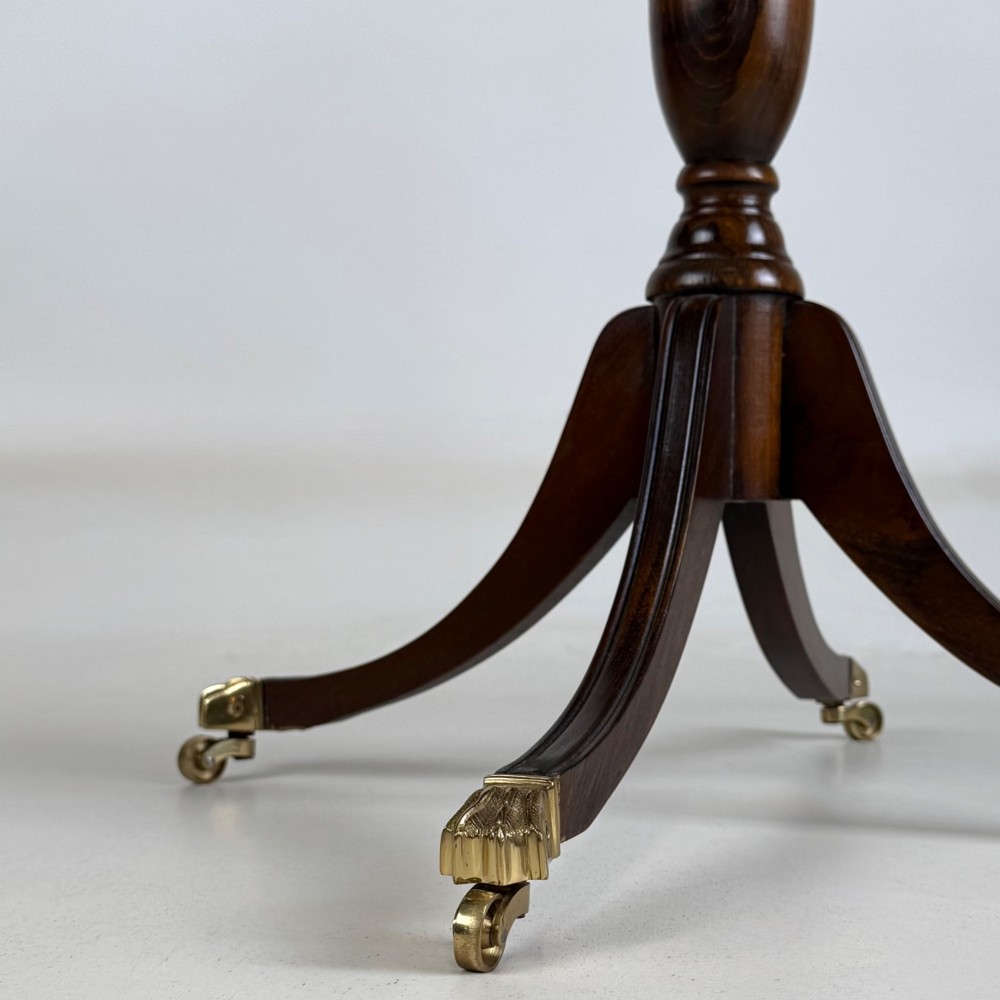 A dark brown oak pedestal side table with an oval top, turned central column, and swept legs featuring brass paw castors. View IX