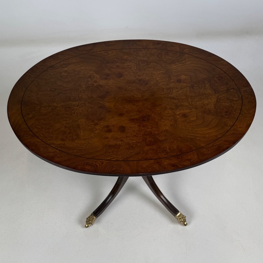 A dark brown oak pedestal side table with an oval top, turned central column, and swept legs featuring brass paw castors. View X