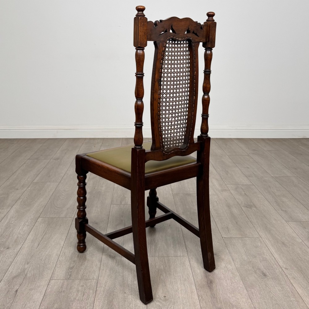 A set of six Victorian oak dining chairs featuring carved crest rails, cane backrest panels, turned legs, and green upholstered seats. View IV