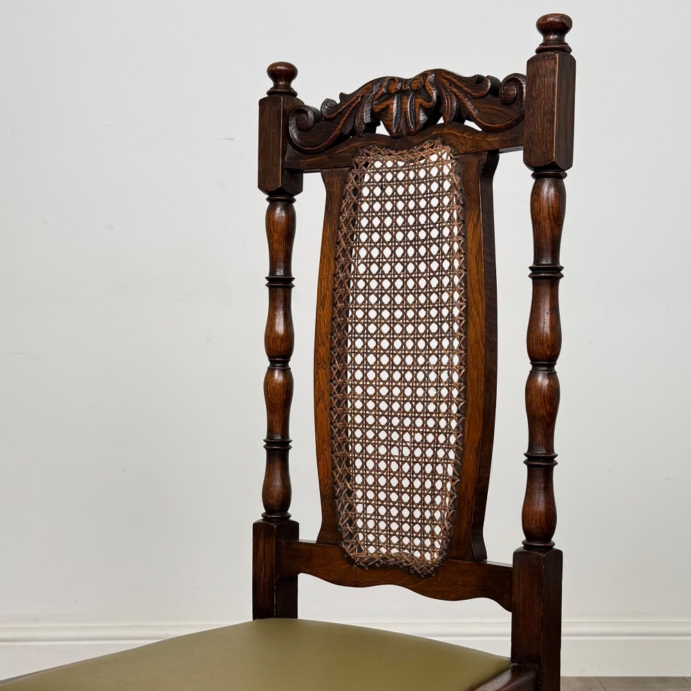 A set of six Victorian oak dining chairs featuring carved crest rails, cane backrest panels, turned legs, and green upholstered seats. View V
