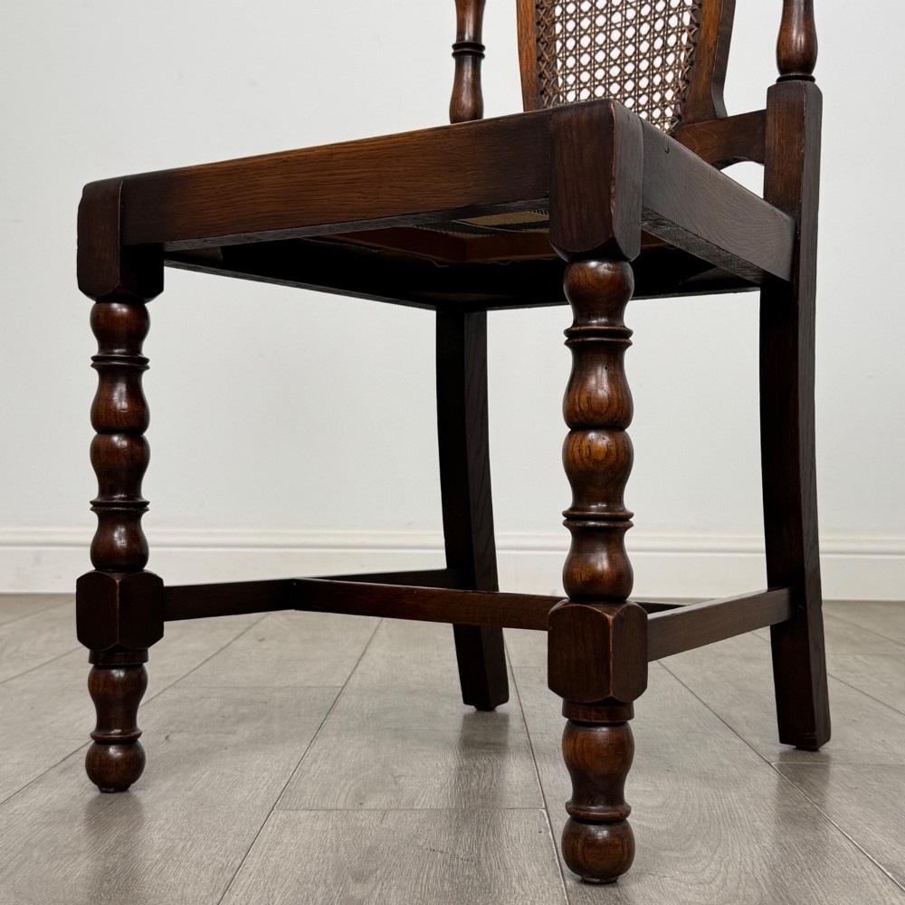 A set of six Victorian oak dining chairs featuring carved crest rails, cane backrest panels, turned legs, and green upholstered seats. View VI