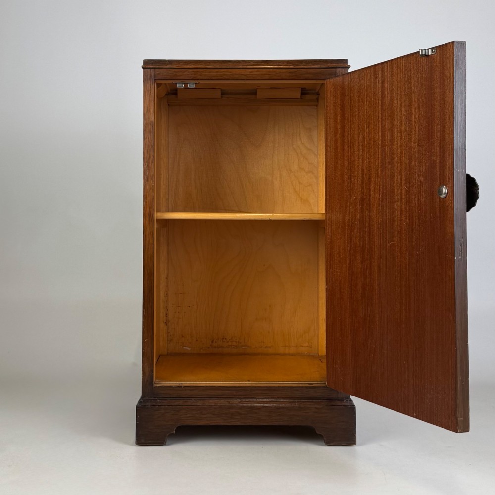 A standing antique dark oak bedside cabinet with a single framed door, a round carved handle, and a solid plinth base. View II
