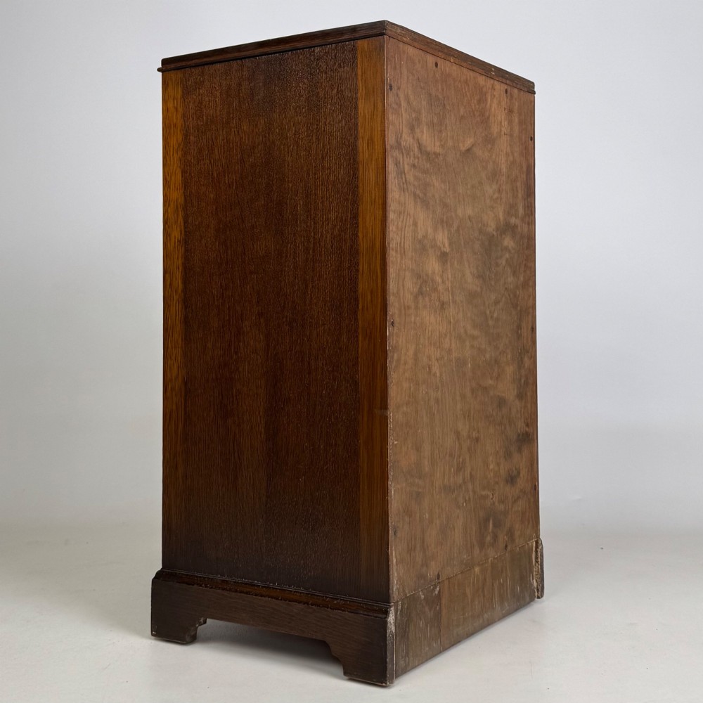 A standing antique dark oak bedside cabinet with a single framed door, a round carved handle, and a solid plinth base. View V