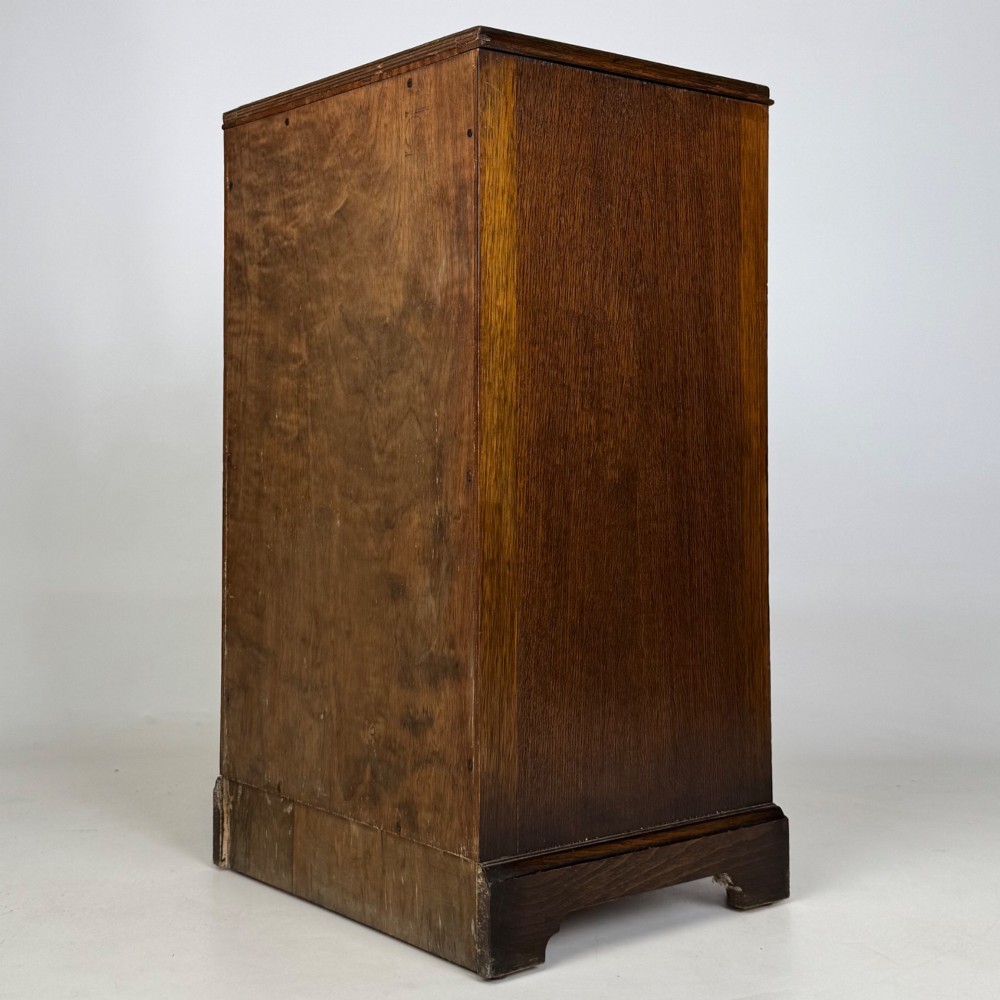 A standing antique dark oak bedside cabinet with a single framed door, a round carved handle, and a solid plinth base. View VII