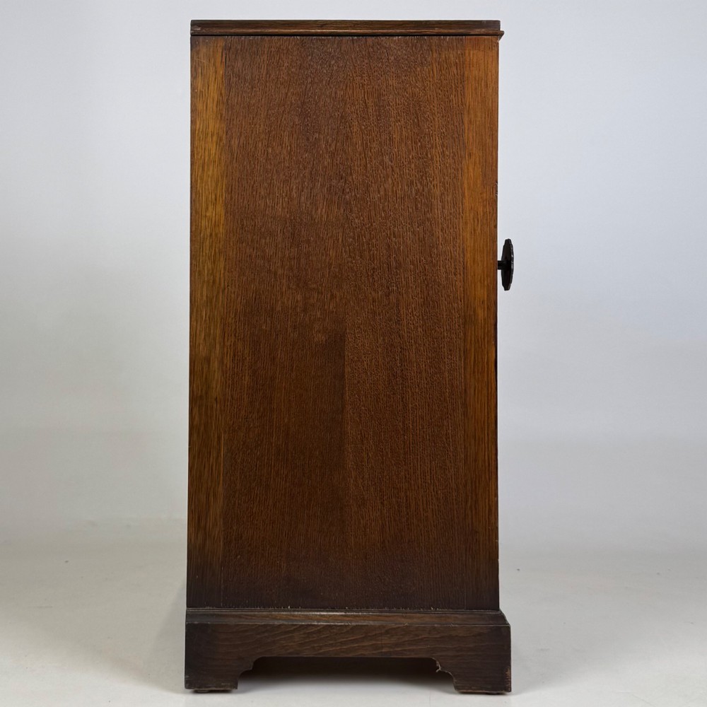 A standing antique dark oak bedside cabinet with a single framed door, a round carved handle, and a solid plinth base. View VIII