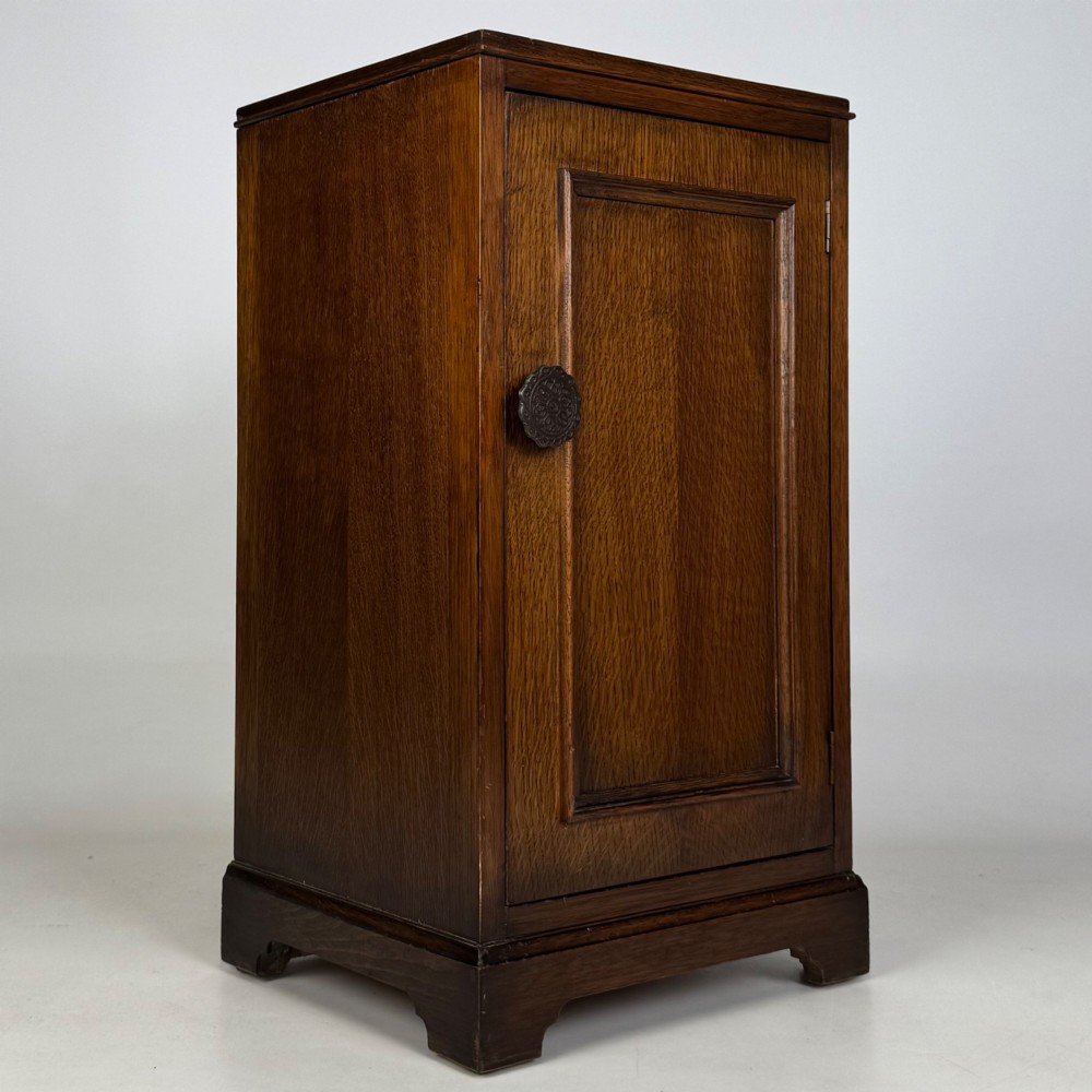 A standing antique dark oak bedside cabinet with a single framed door, a round carved handle, and a solid plinth base. View IX