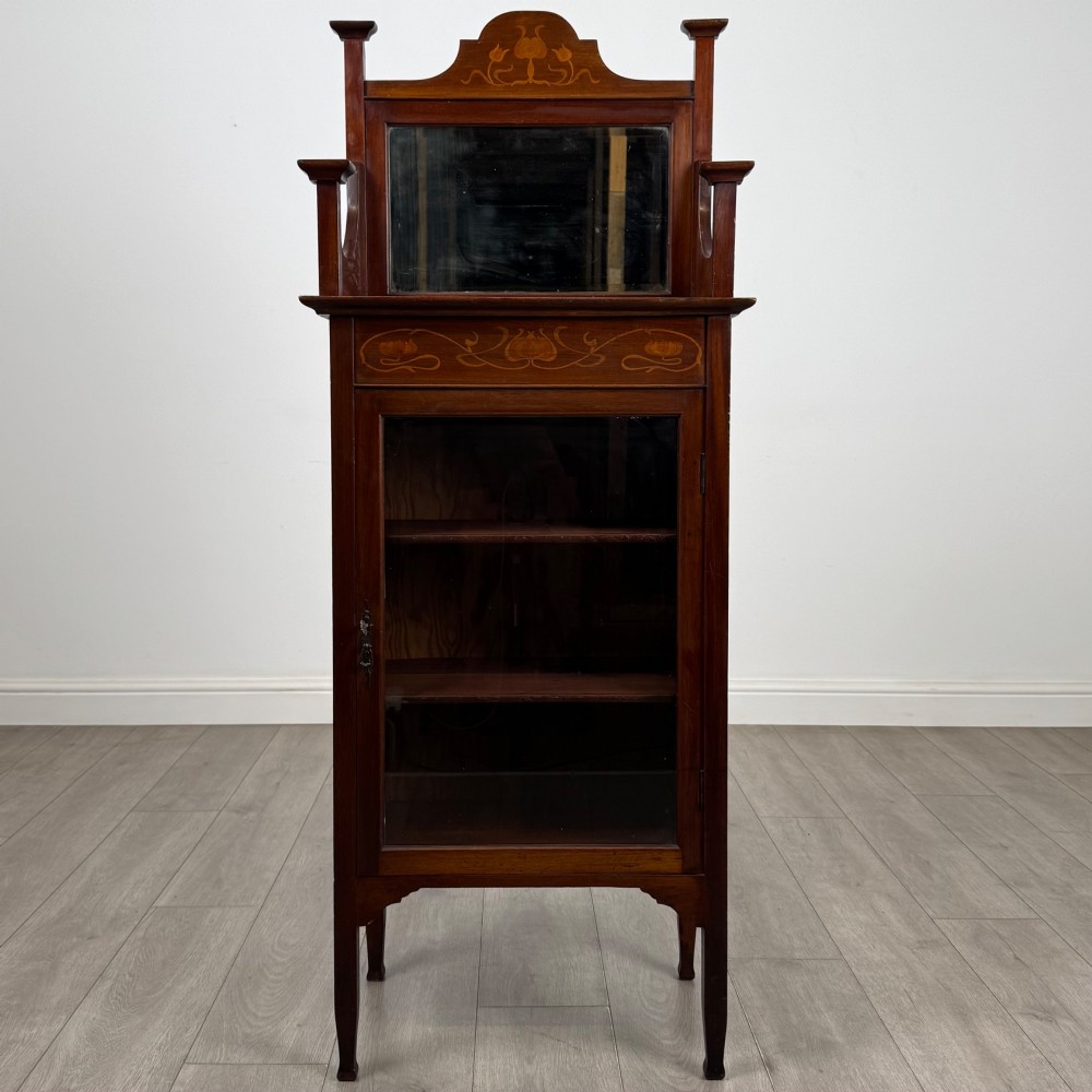 An Edwardian mahogany display cabinet featuring a upper mirrored rail with floral wood inlay above a single glazed door cupboard.
