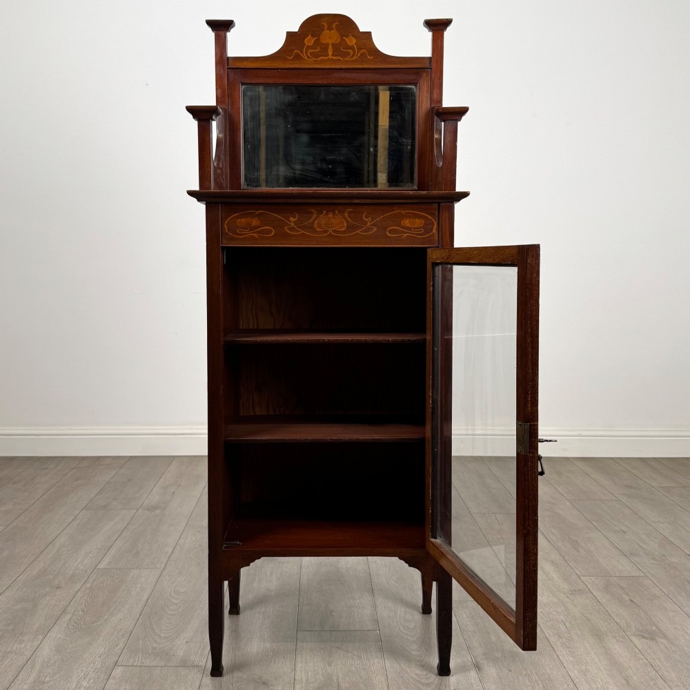 An Edwardian mahogany display cabinet featuring a upper mirrored rail with floral wood inlay above a single glazed door cupboard. View II