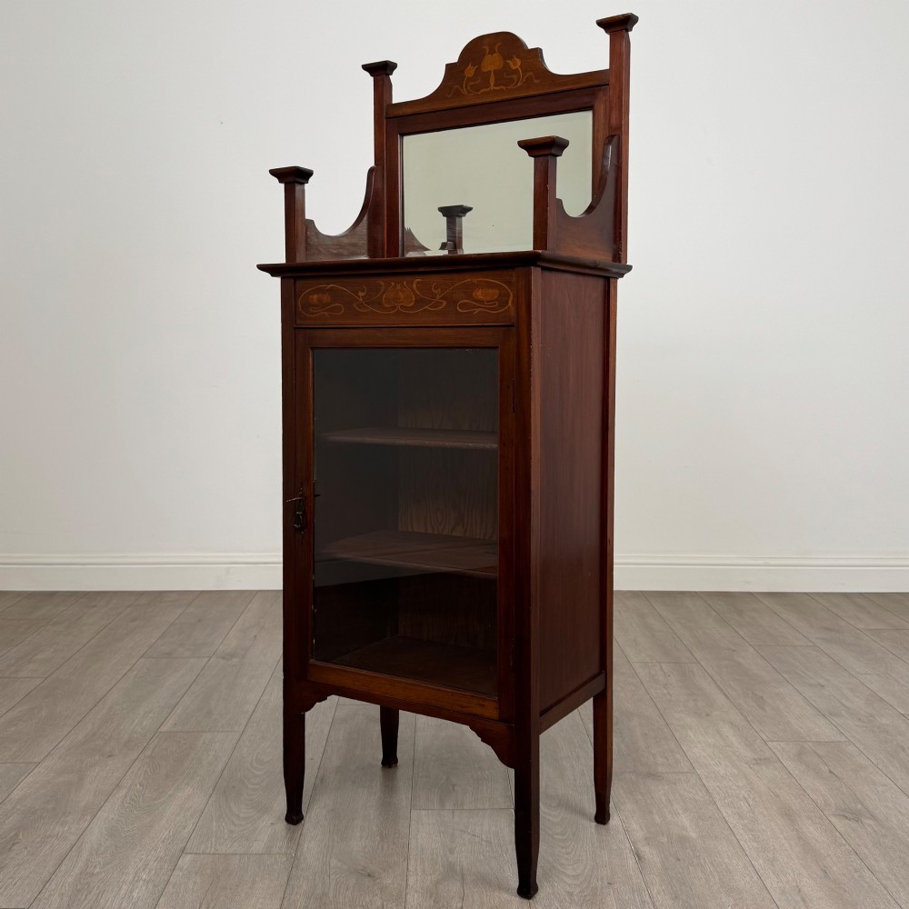 An Edwardian mahogany display cabinet featuring a upper mirrored rail with floral wood inlay above a single glazed door cupboard. View III