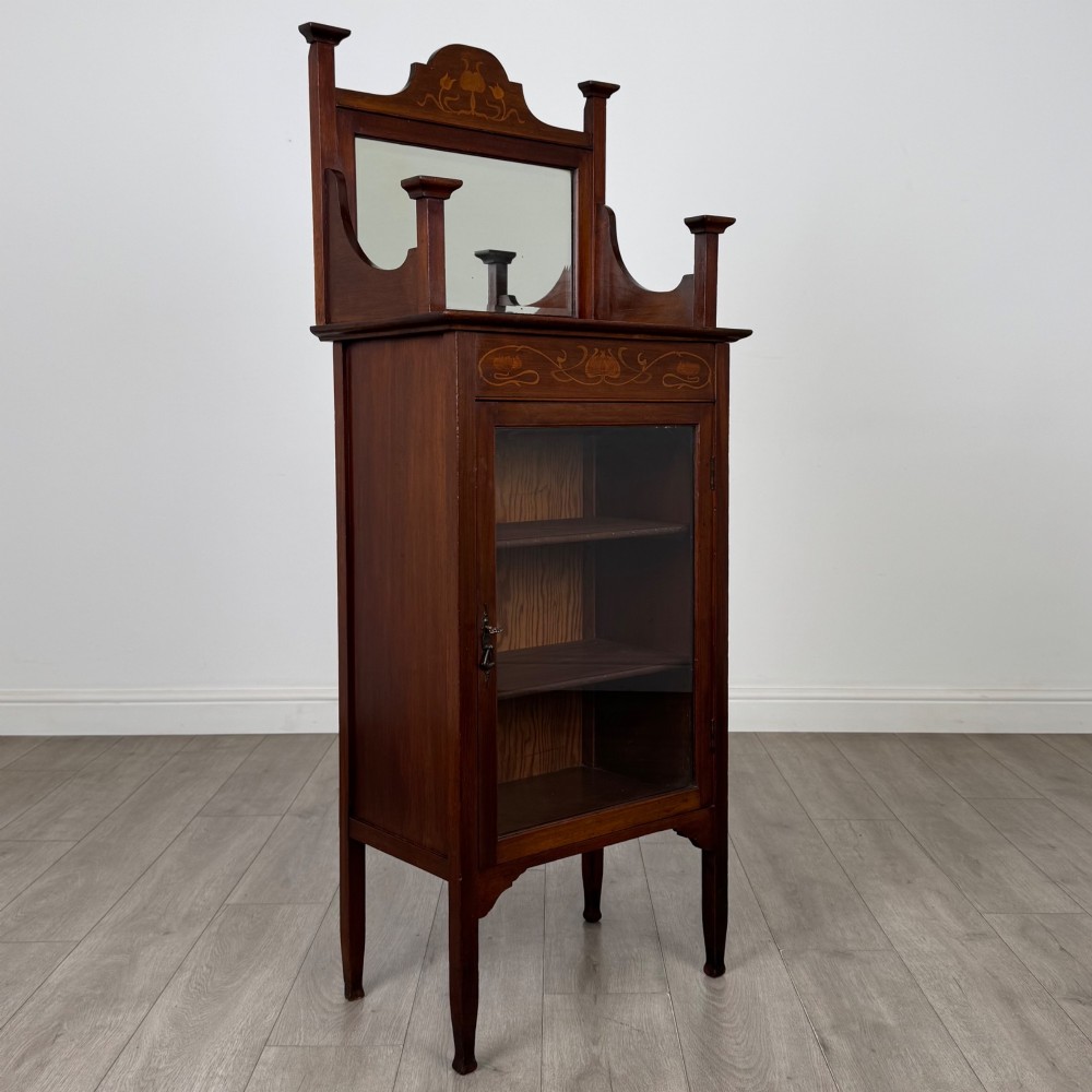 An Edwardian mahogany display cabinet featuring a upper mirrored rail with floral wood inlay above a single glazed door cupboard. View IX