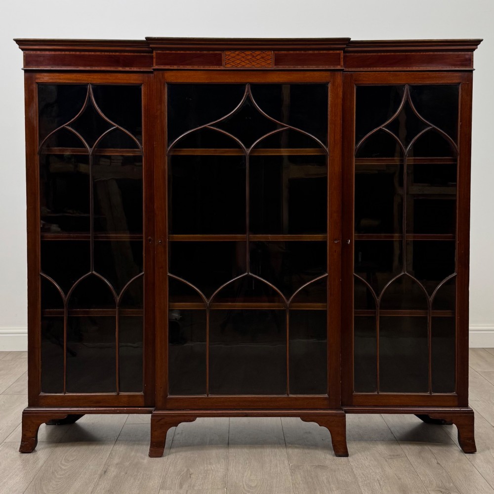 A Victorian mahogany breakfront display cabinet with three astragal glazed doors featuring gothic arch tracery and top frieze inlay.