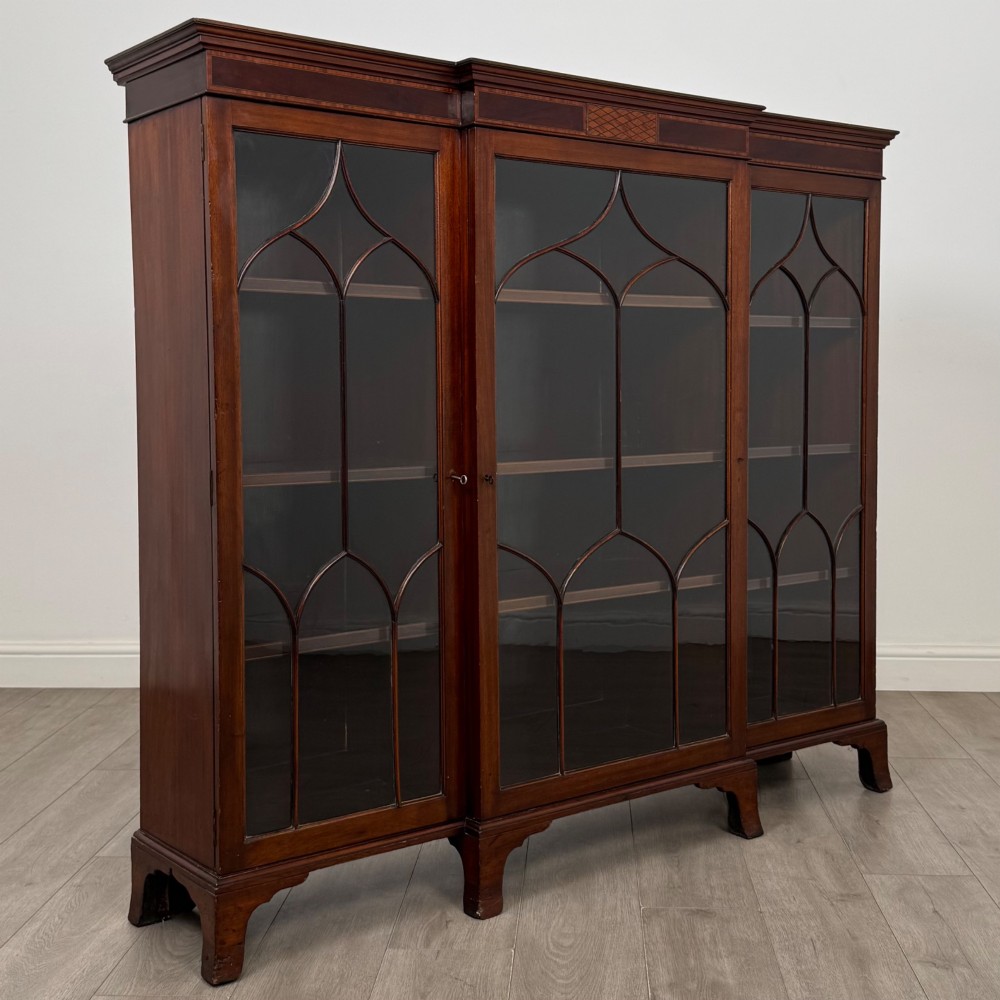 A Victorian mahogany breakfront display cabinet with three astragal glazed doors featuring gothic arch tracery and top frieze inlay. View IX