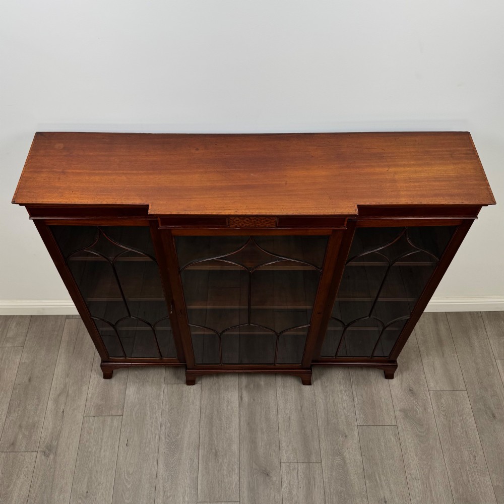 A Victorian mahogany breakfront display cabinet with three astragal glazed doors featuring gothic arch tracery and top frieze inlay. View X