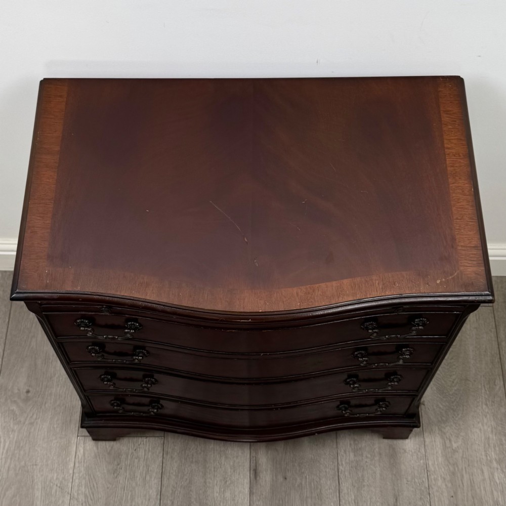 A mahogany serpentine-front chest of drawers featuring four graduated drawers with brass handles and bracket feet. View IX