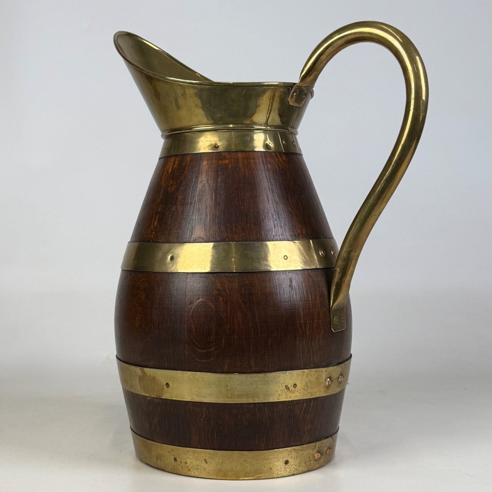 A tall dark oak wooden jug styled as an umbrella stand, featuring decorative brass bands, a curved brass handle, and a brass spout. View III