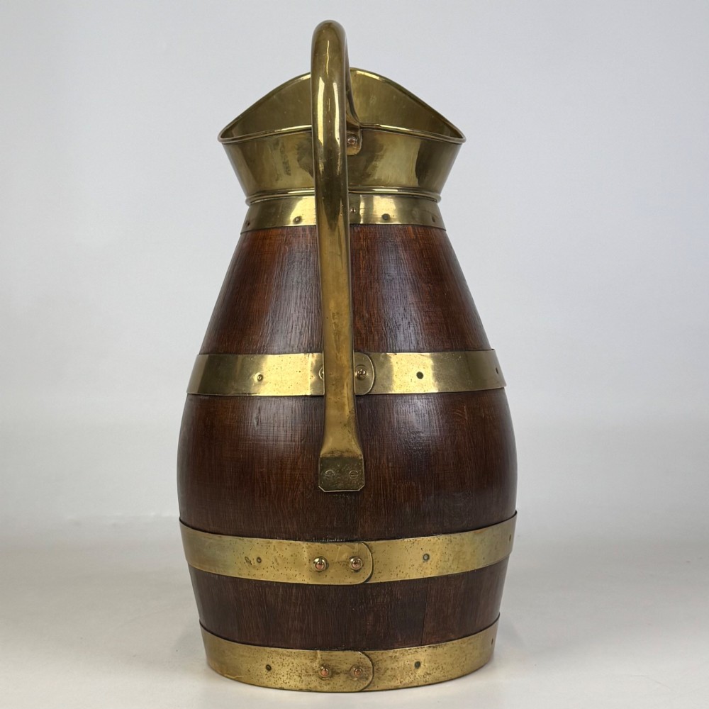A tall dark oak wooden jug styled as an umbrella stand, featuring decorative brass bands, a curved brass handle, and a brass spout. View IV