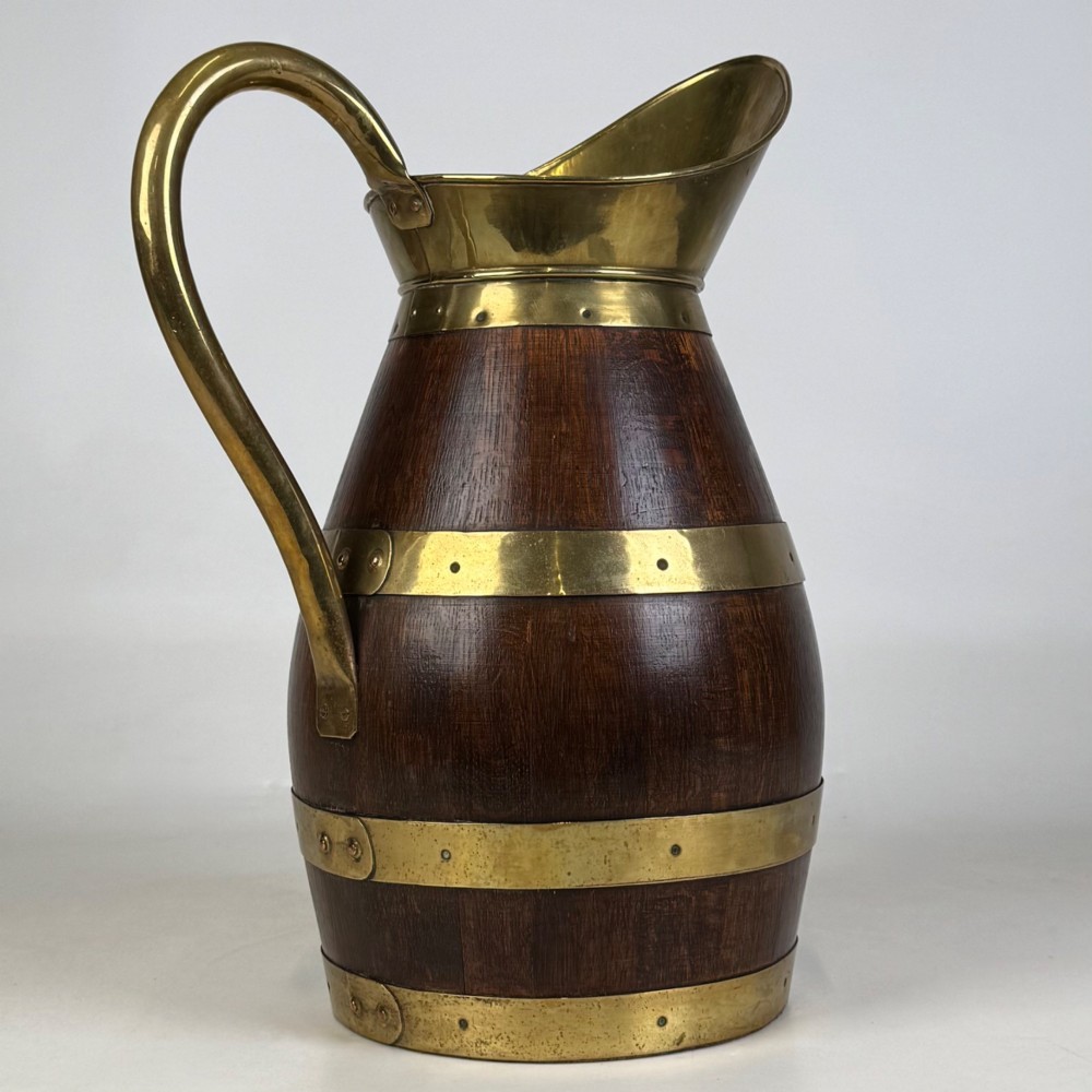 A tall dark oak wooden jug styled as an umbrella stand, featuring decorative brass bands, a curved brass handle, and a brass spout. View V