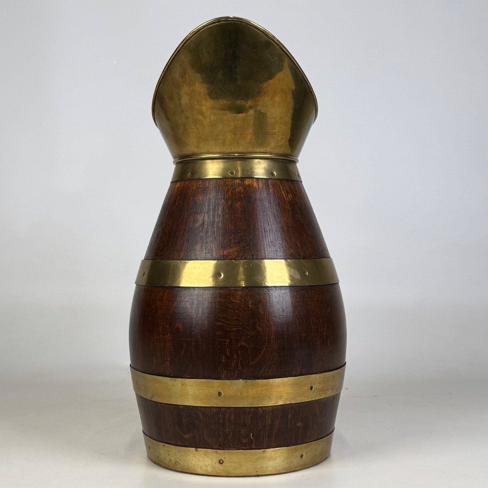 A tall dark oak wooden jug styled as an umbrella stand, featuring decorative brass bands, a curved brass handle, and a brass spout. View VIII