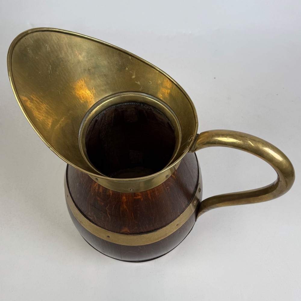 A tall dark oak wooden jug styled as an umbrella stand, featuring decorative brass bands, a curved brass handle, and a brass spout. View IX